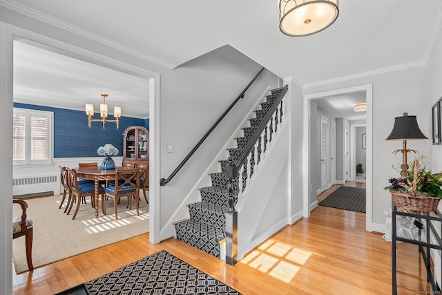 staircase with crown molding, radiator heating unit, wood-type flooring, and a notable chandelier