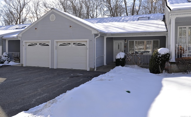 snow covered property with a porch and a garage