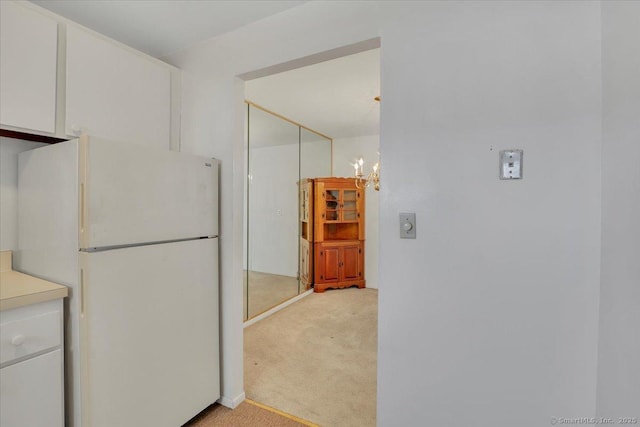 kitchen with white refrigerator, a notable chandelier, light carpet, and white cabinets