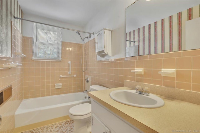 full bathroom with tile walls, vanity, tiled shower / bath, and toilet