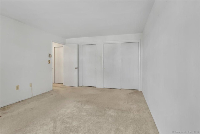 unfurnished bedroom featuring two closets and light colored carpet