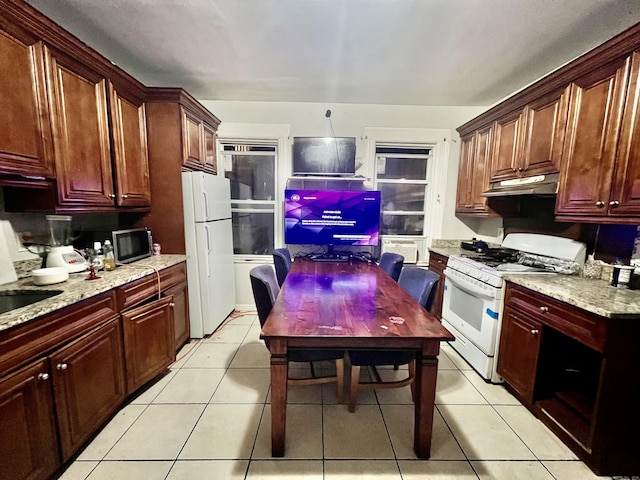 kitchen with under cabinet range hood, light tile patterned floors, white appliances, and light stone counters