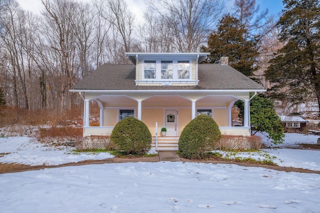 bungalow-style house featuring roof with shingles, a porch, and a chimney