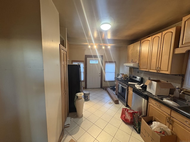 kitchen featuring tasteful backsplash, sink, light tile patterned floors, stainless steel gas range oven, and black fridge