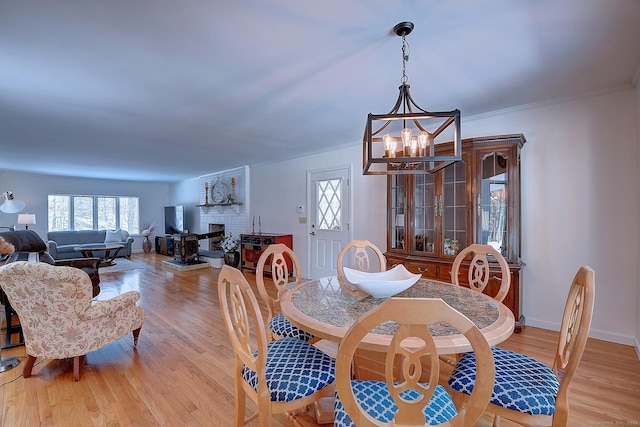 dining space featuring ornamental molding, a brick fireplace, an inviting chandelier, and light hardwood / wood-style floors