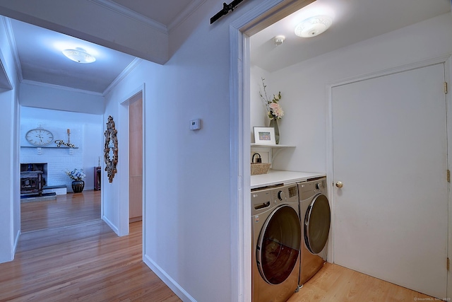 laundry room with a barn door, ornamental molding, separate washer and dryer, and light wood-type flooring