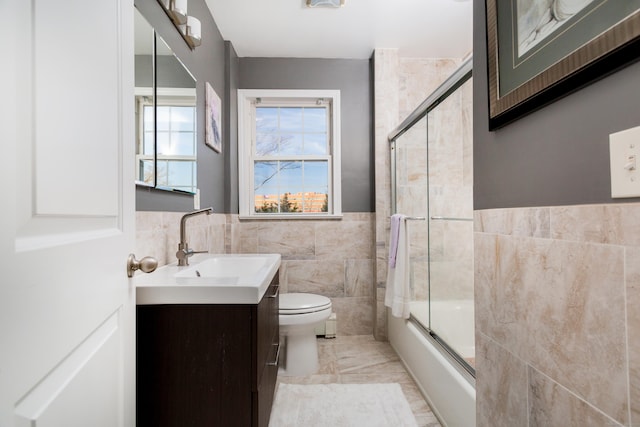 full bathroom featuring tile walls, vanity, toilet, and combined bath / shower with glass door