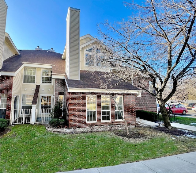 view of home's exterior featuring a shingled roof, brick siding, a lawn, and a chimney