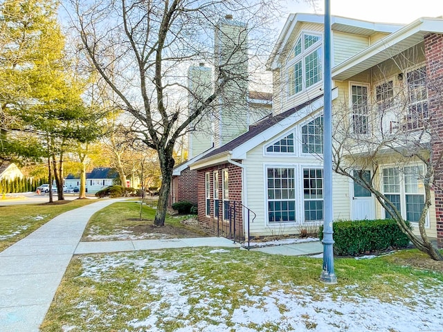 snow covered property featuring a chimney, a lawn, and brick siding