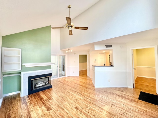 unfurnished living room with lofted ceiling, ceiling fan, a fireplace, visible vents, and light wood-type flooring