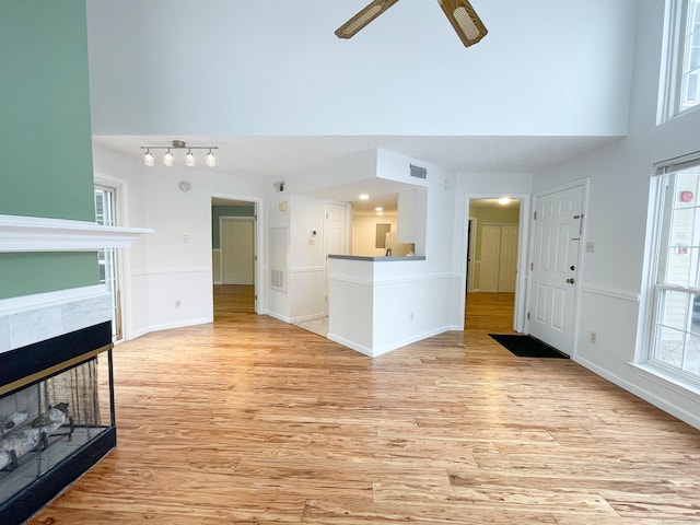 unfurnished living room with light wood finished floors, a high ceiling, visible vents, and a tiled fireplace