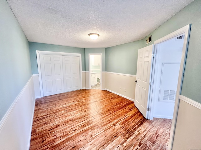 unfurnished bedroom featuring light wood-type flooring, a closet, wainscoting, and a textured ceiling