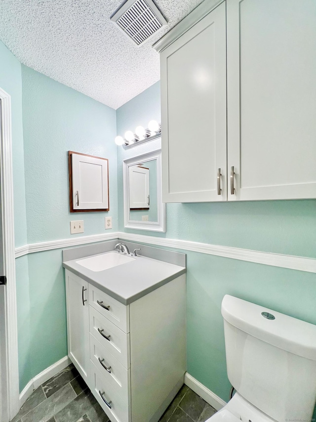 half bath featuring visible vents, toilet, vanity, a textured ceiling, and baseboards