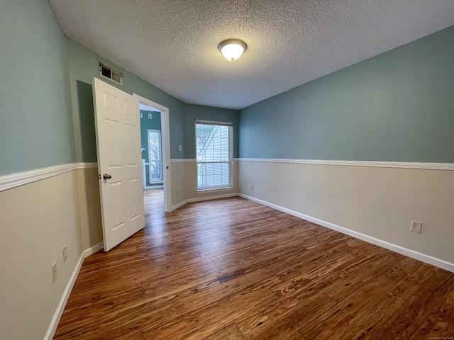 unfurnished room featuring a textured ceiling, wood finished floors, visible vents, and baseboards