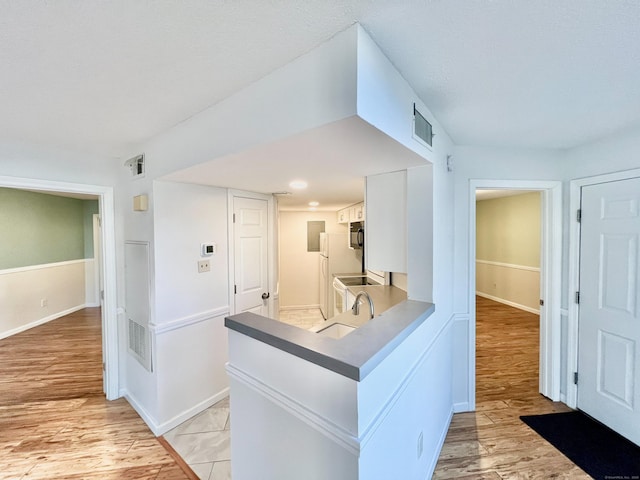 hall featuring light wood-type flooring, visible vents, a sink, and baseboards