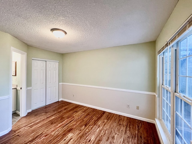 unfurnished bedroom featuring a closet, a textured ceiling, baseboards, and wood finished floors