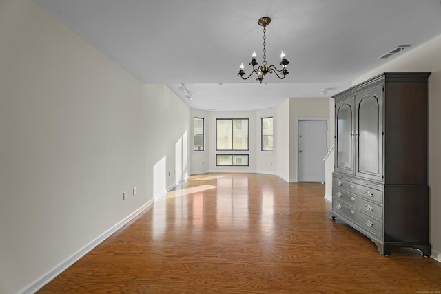 unfurnished living room with track lighting, wood-type flooring, and a notable chandelier