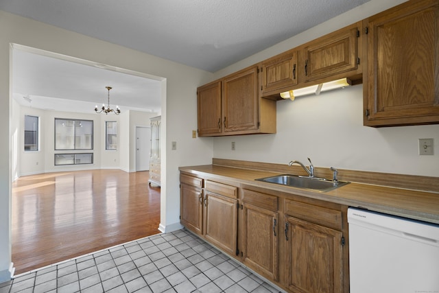 kitchen featuring sink, light tile patterned floors, white dishwasher, decorative light fixtures, and a chandelier