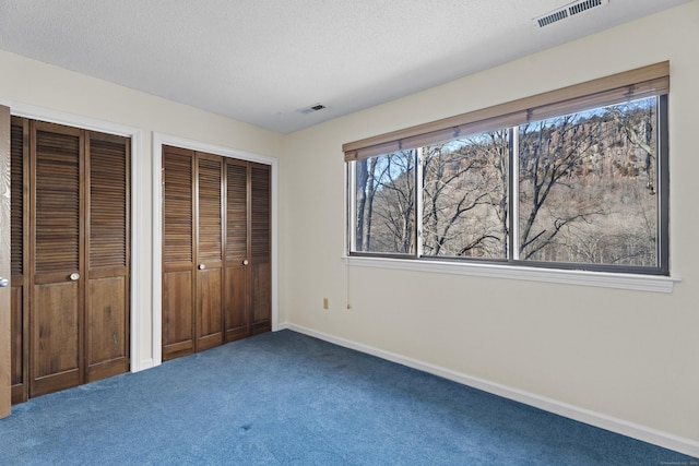 unfurnished bedroom featuring two closets, a textured ceiling, and carpet