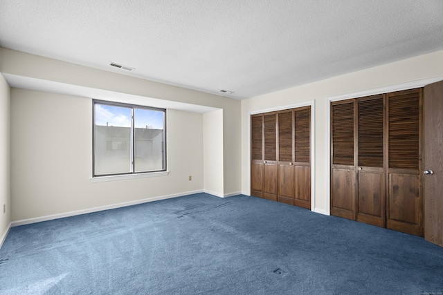 unfurnished bedroom featuring multiple closets, carpet flooring, and a textured ceiling