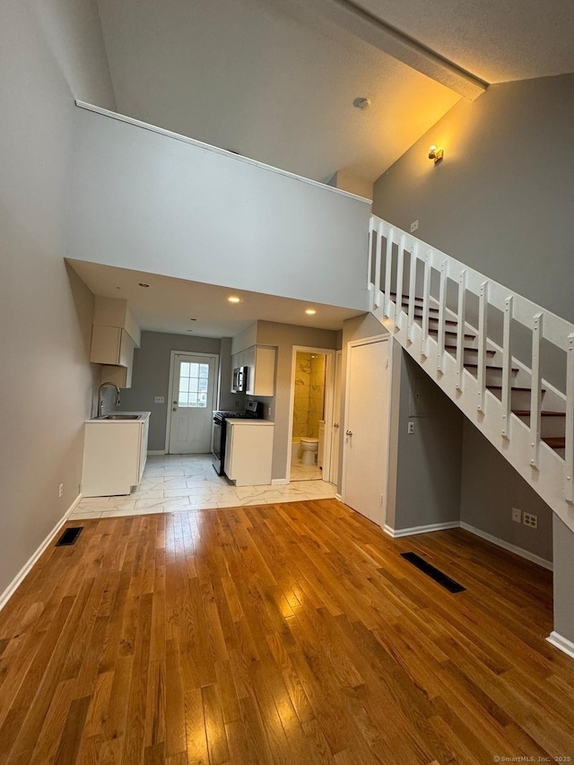 unfurnished living room featuring high vaulted ceiling, sink, and light wood-type flooring