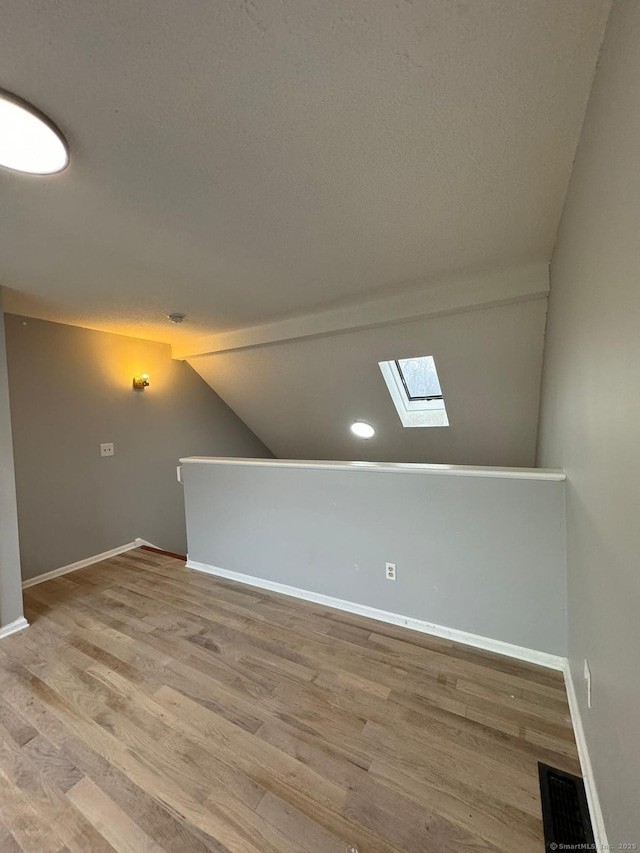 additional living space with lofted ceiling with skylight, light hardwood / wood-style flooring, and a textured ceiling