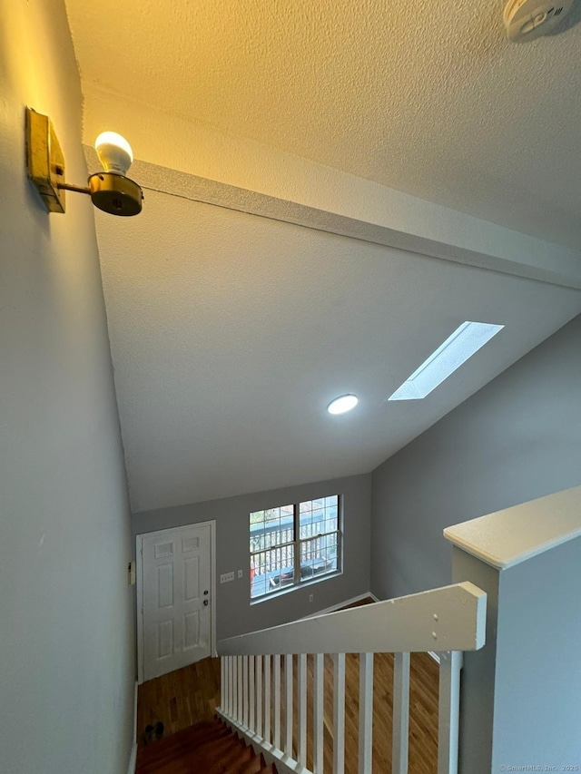 staircase with lofted ceiling with beams, hardwood / wood-style floors, and a textured ceiling