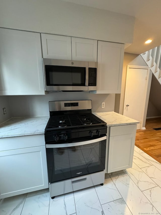 kitchen with white cabinetry, appliances with stainless steel finishes, and light stone counters