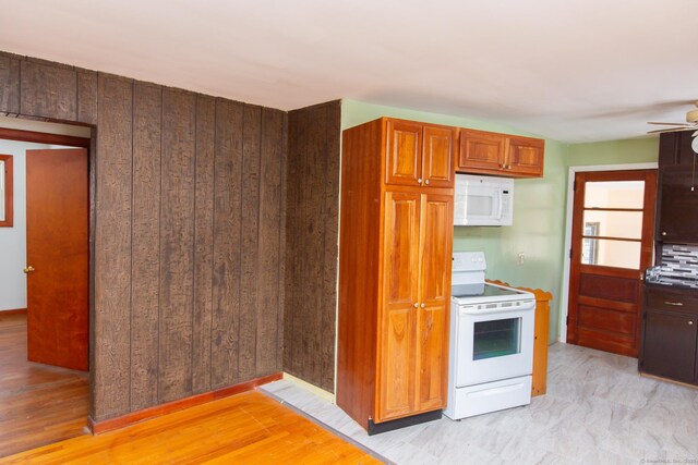 kitchen featuring ceiling fan, light wood-type flooring, wooden walls, and white appliances