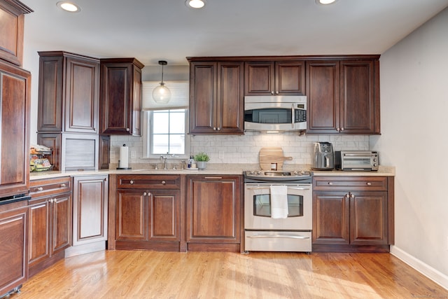 kitchen featuring appliances with stainless steel finishes, sink, decorative backsplash, hanging light fixtures, and light wood-type flooring