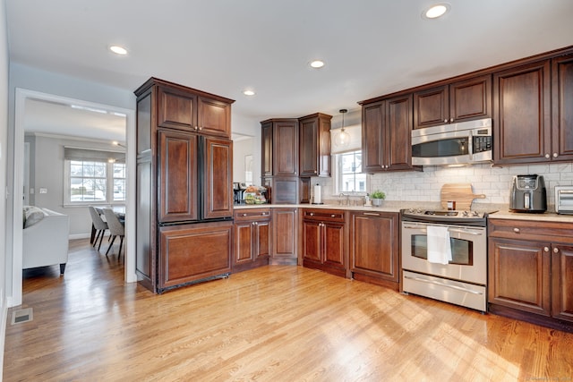 kitchen with hanging light fixtures, decorative backsplash, light hardwood / wood-style floors, and appliances with stainless steel finishes