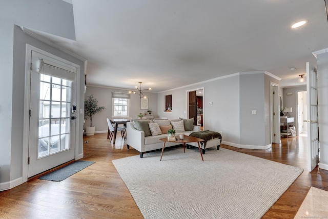 living room with a notable chandelier, ornamental molding, and light wood-type flooring