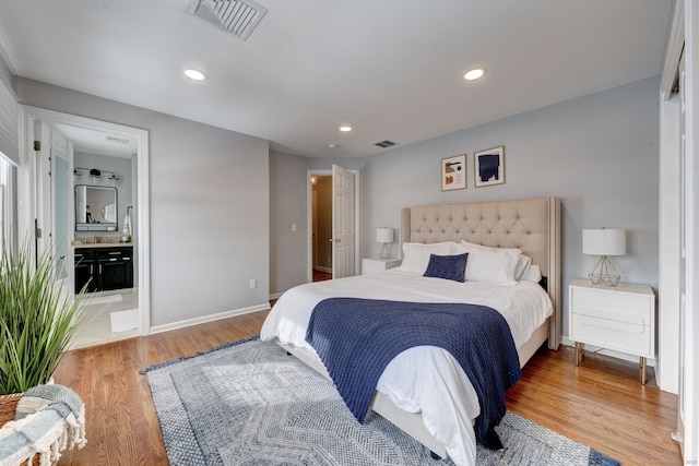 bedroom featuring hardwood / wood-style flooring, ensuite bathroom, and sink