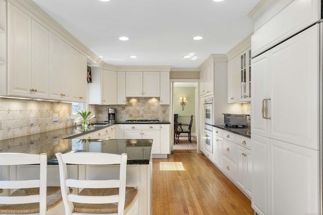 kitchen featuring dark countertops, light wood-style flooring, a peninsula, and glass insert cabinets