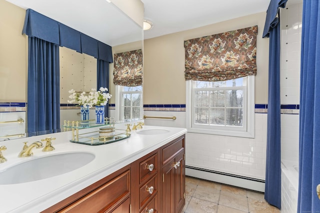 full bathroom with a baseboard heating unit, double vanity, a sink, and tile walls