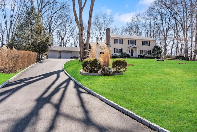 view of front of home with a garage, a front lawn, a chimney, and an outdoor structure