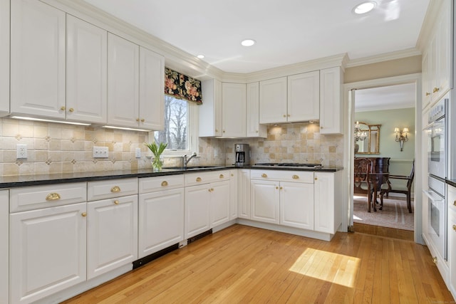 kitchen with tasteful backsplash, white cabinets, white double oven, ornamental molding, and light wood-style floors