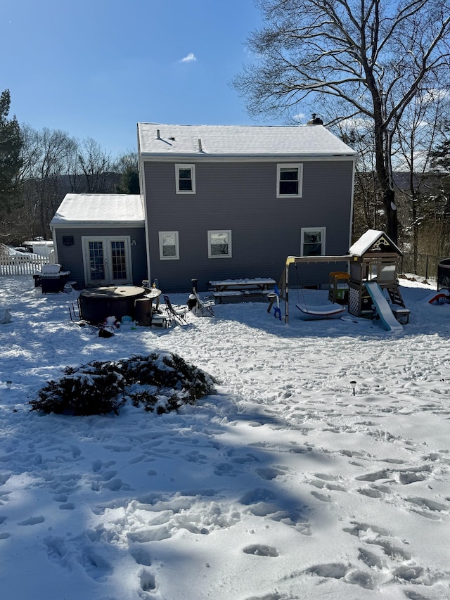 snow covered house featuring a jacuzzi, french doors, and a playground