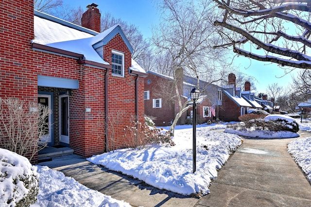 snow covered property featuring brick siding and a chimney