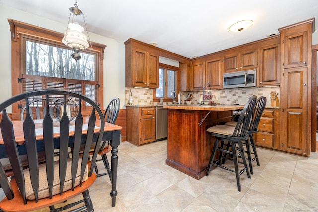 kitchen featuring a kitchen island, light countertops, appliances with stainless steel finishes, brown cabinets, and decorative backsplash