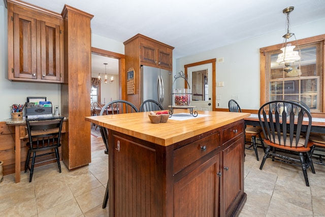 kitchen featuring pendant lighting, butcher block counters, a kitchen island, a chandelier, and stainless steel refrigerator