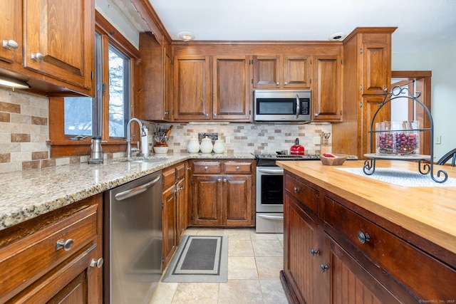 kitchen with brown cabinets, stainless steel appliances, tasteful backsplash, butcher block counters, and a sink