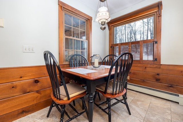 dining area with a baseboard radiator, wainscoting, and wood walls