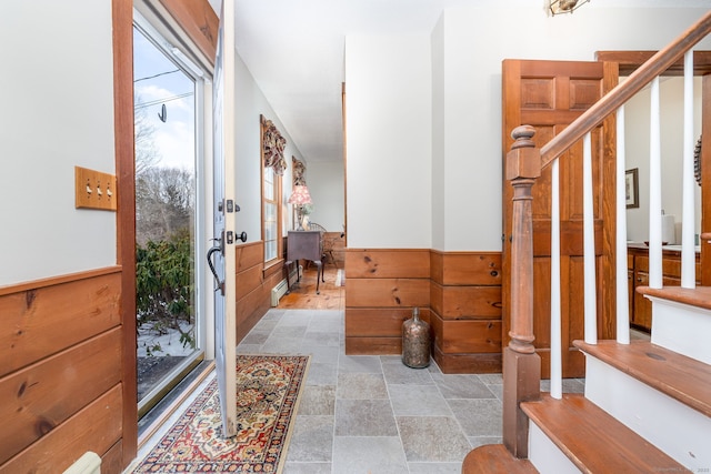 entrance foyer with stairway, wood walls, wainscoting, and stone finish floor