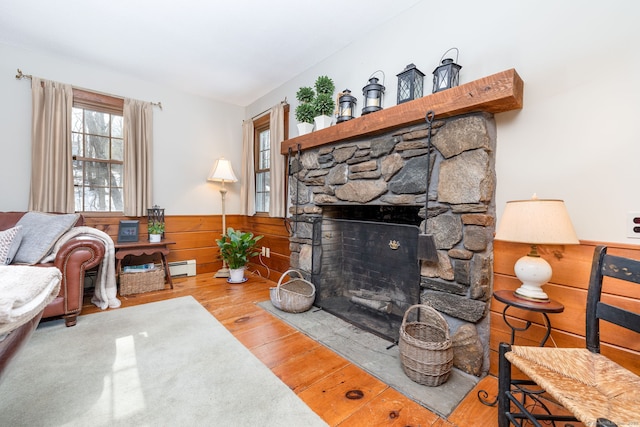 living room featuring wainscoting, wood finished floors, and a stone fireplace