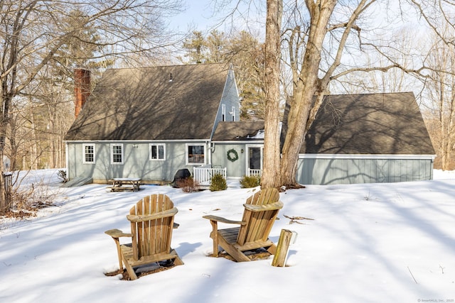 snow covered house featuring roof with shingles and a chimney