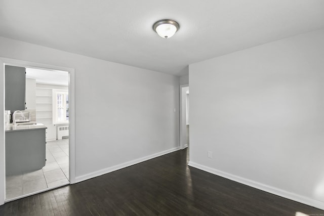 unfurnished room with wood-type flooring, sink, and radiator heating unit