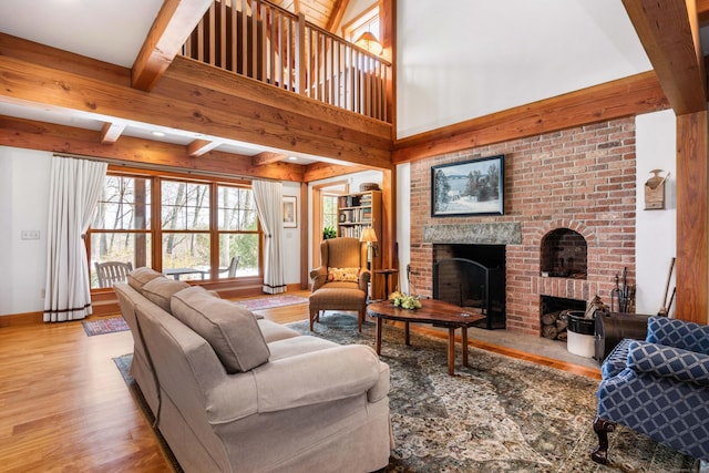 living area featuring baseboards, beamed ceiling, a fireplace, a high ceiling, and wood finished floors