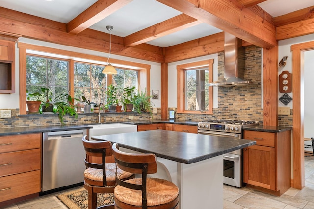 kitchen with dark countertops, beamed ceiling, stainless steel appliances, wall chimney exhaust hood, and a sink