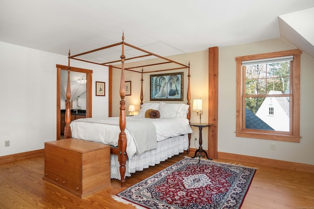 bedroom with vaulted ceiling, wood finished floors, and baseboards